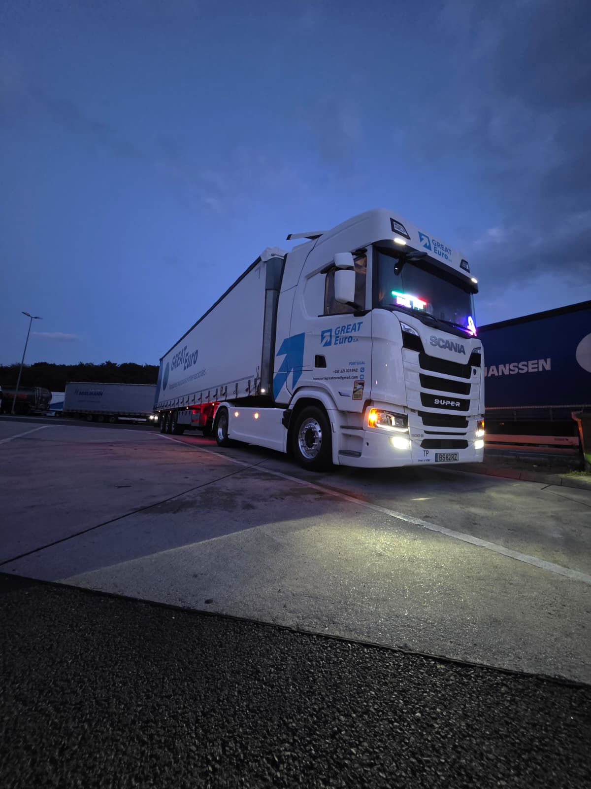 Scania branco com as luzes acesas ao anoitecer